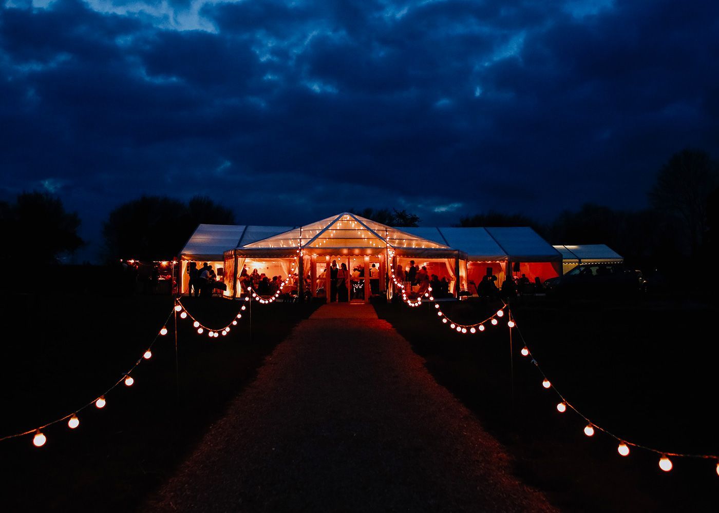 A large tent is lit up at night with people standing underneath it.