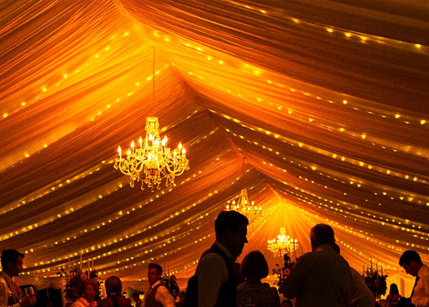 A group of people are dancing under a tent with lights hanging from the ceiling