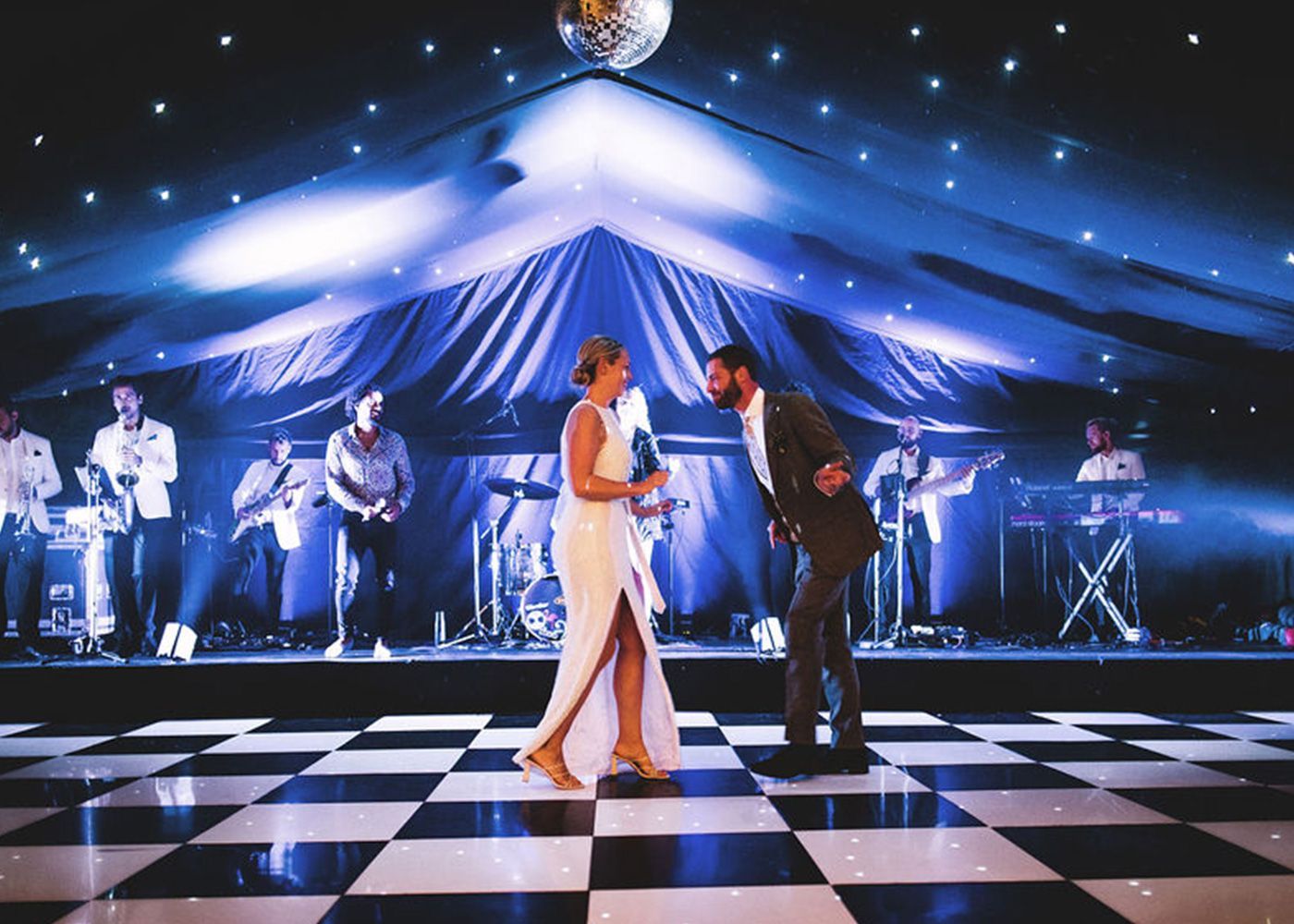 A bride and groom are dancing on a checkered dance floor.
