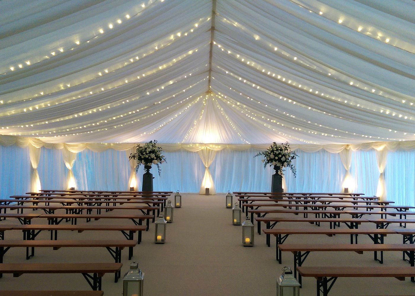 The inside of a tent with rows of benches and lanterns.