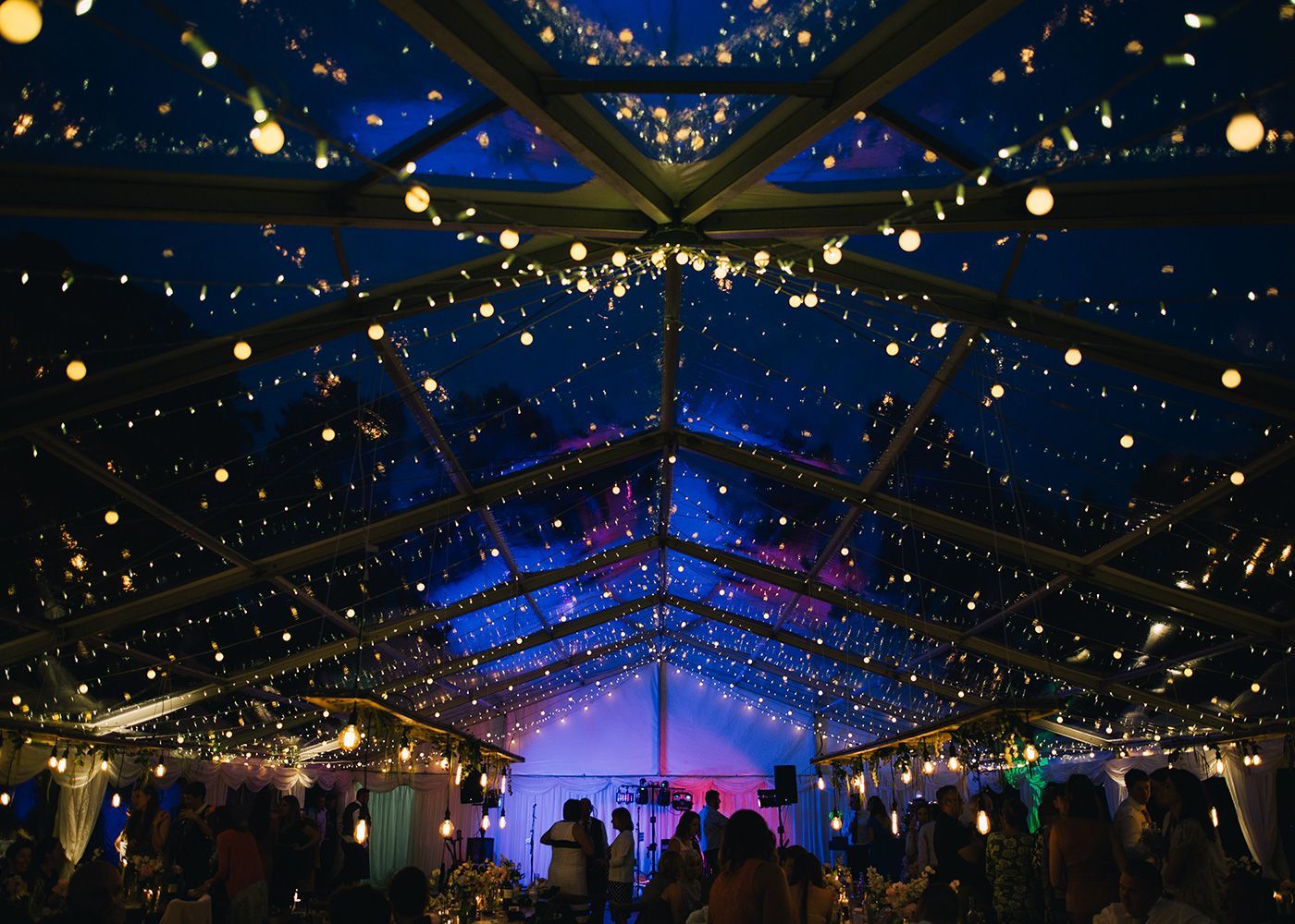 A crowd of people are dancing under a clear tent at night.