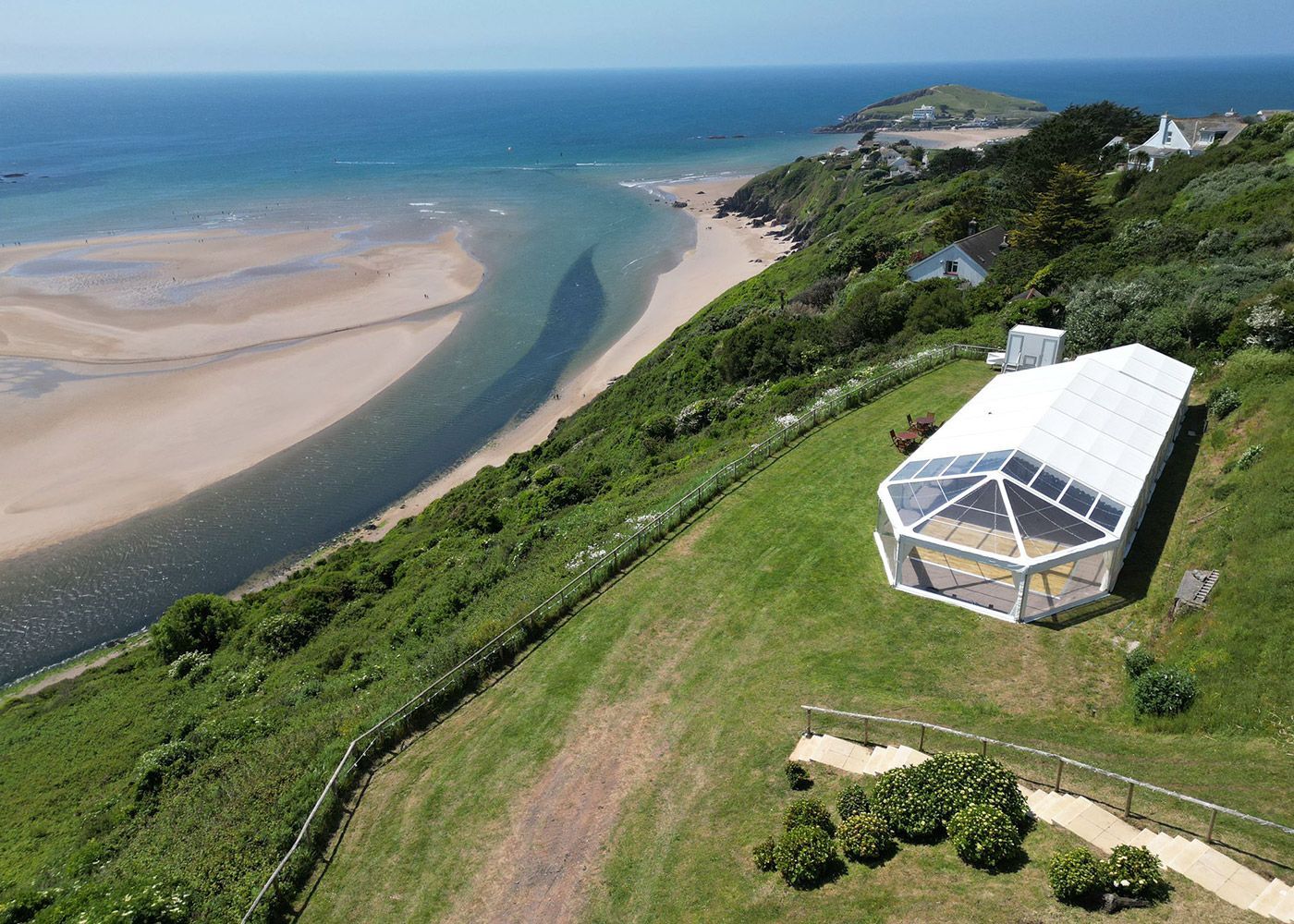 An aerial view of a large tent on a hill overlooking the ocean.