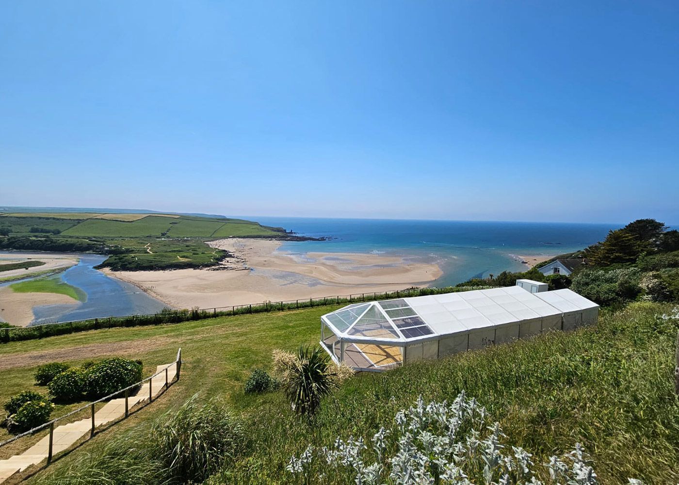 A clear tent is sitting on top of a grassy hill overlooking the ocean.