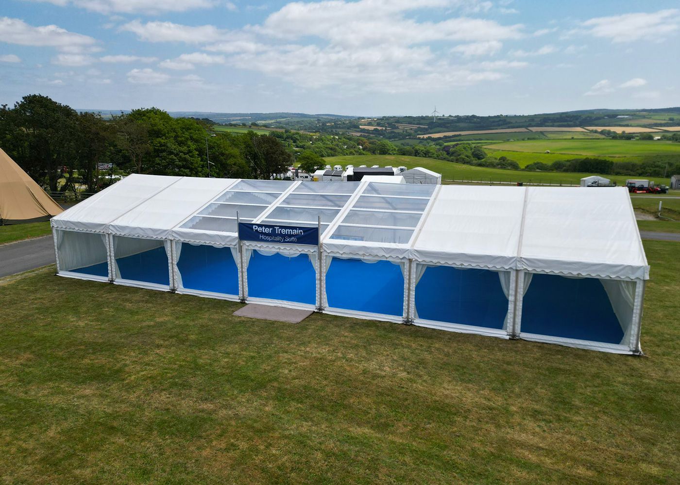 A large white tent with blue curtains is sitting on top of a lush green field.
