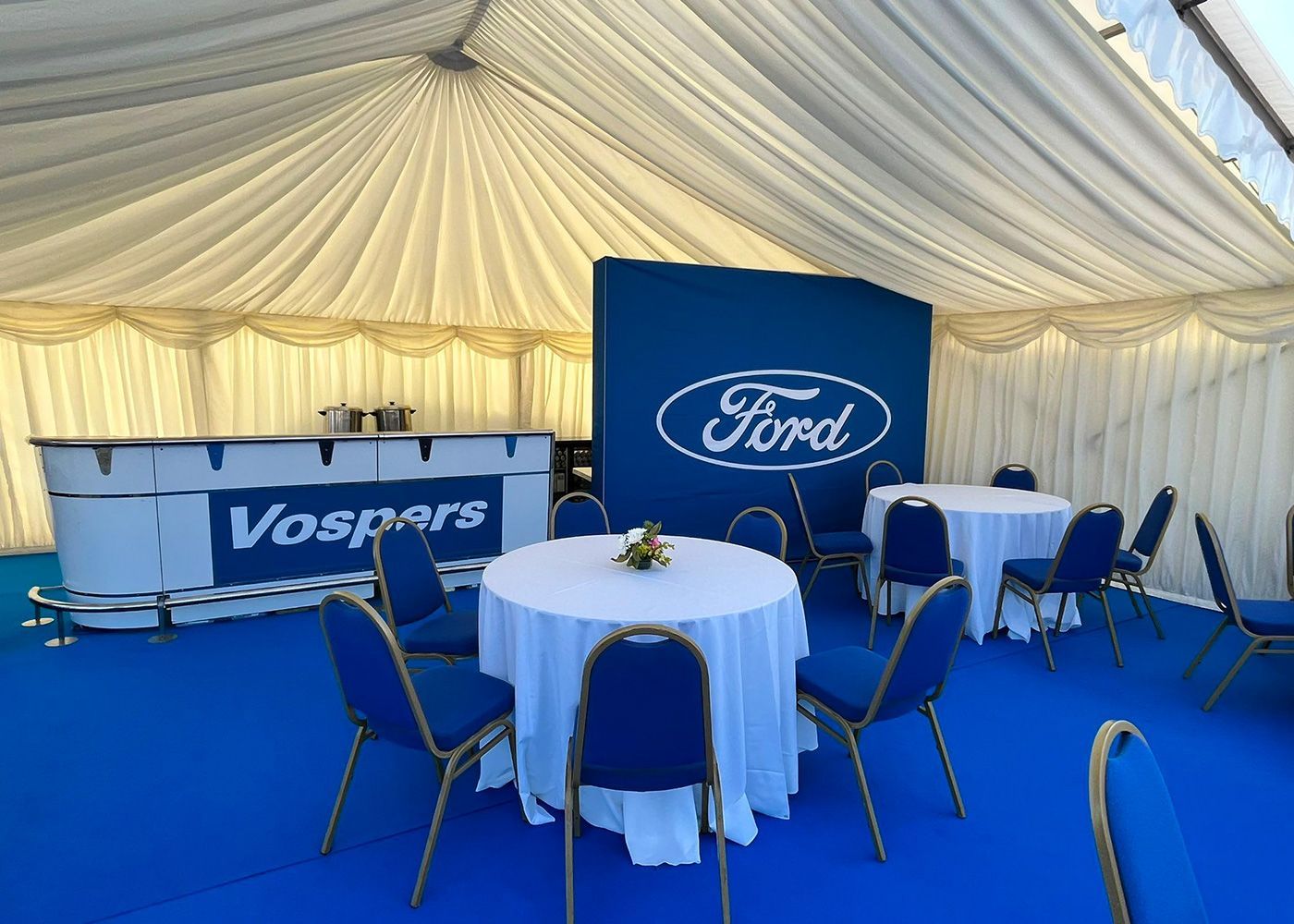 A tent with tables and chairs and a ford logo on the wall.