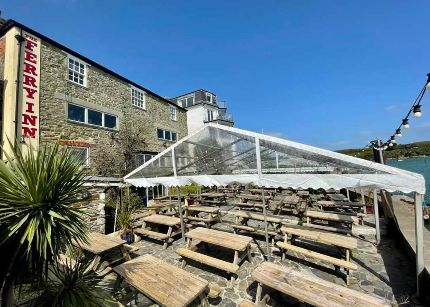 A clear tent is sitting in front of a building with wooden picnic tables.