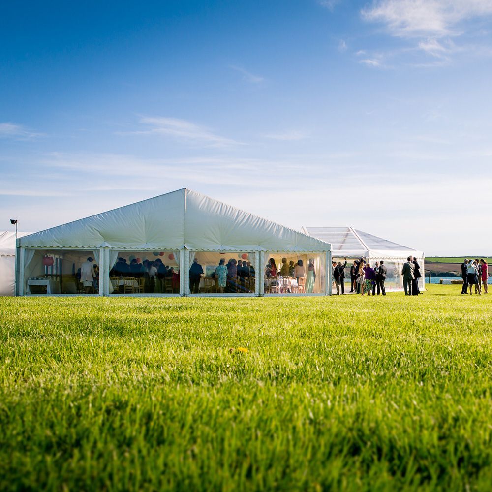 A group of people are standing in a grassy field in front of a large tent.