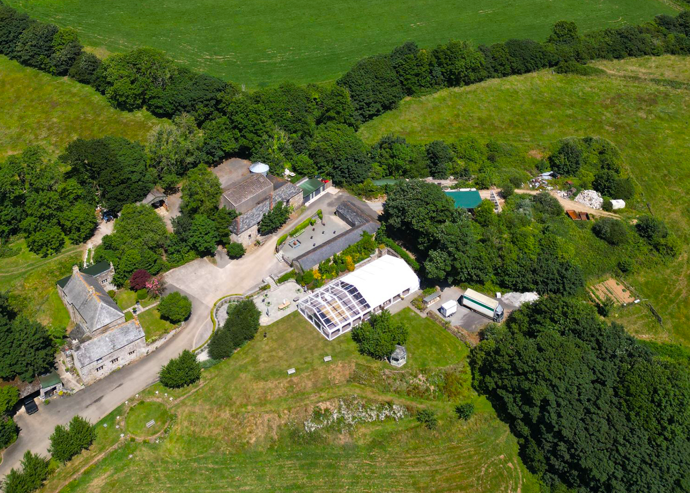 An aerial view of a farm with a large white tent in the middle of the field.
