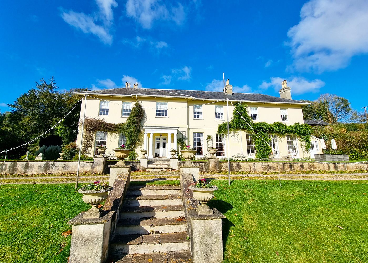 A large white house is sitting on top of a lush green field.