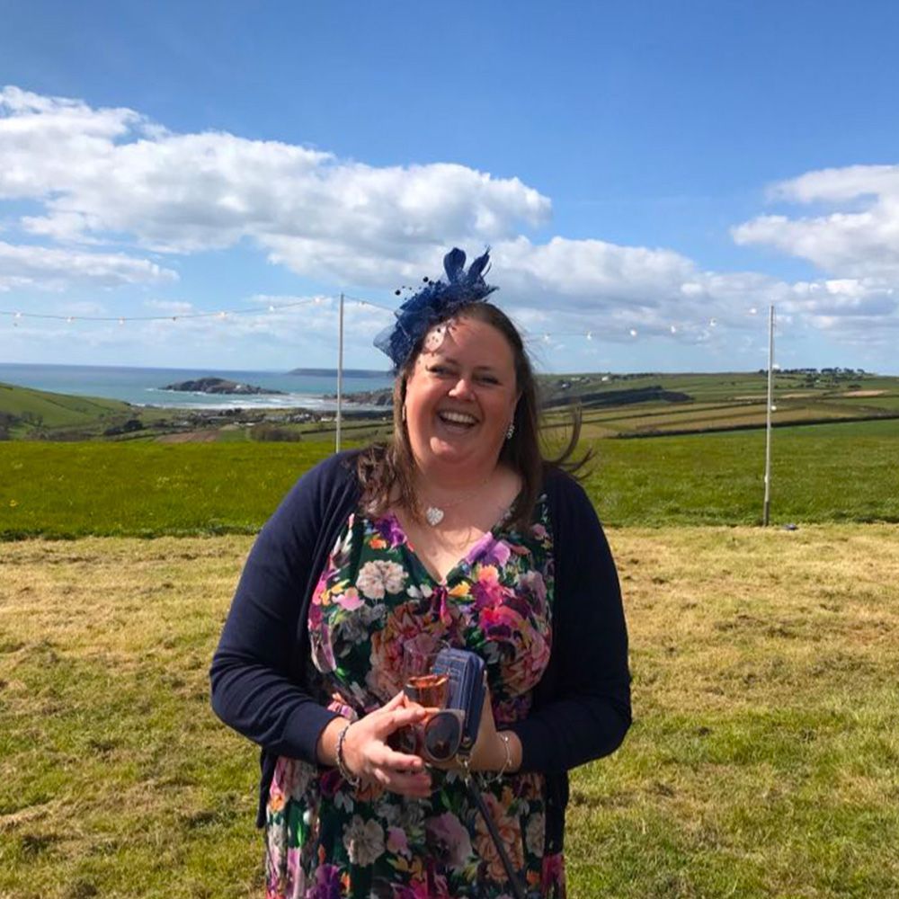 A woman in a floral dress is standing in a field holding a glass of wine.