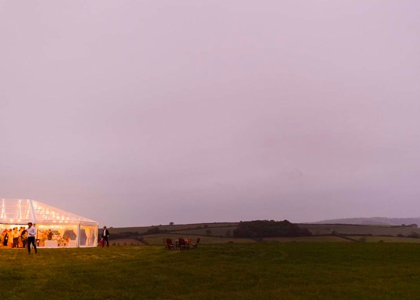A group of people are standing in a field in front of a tent.