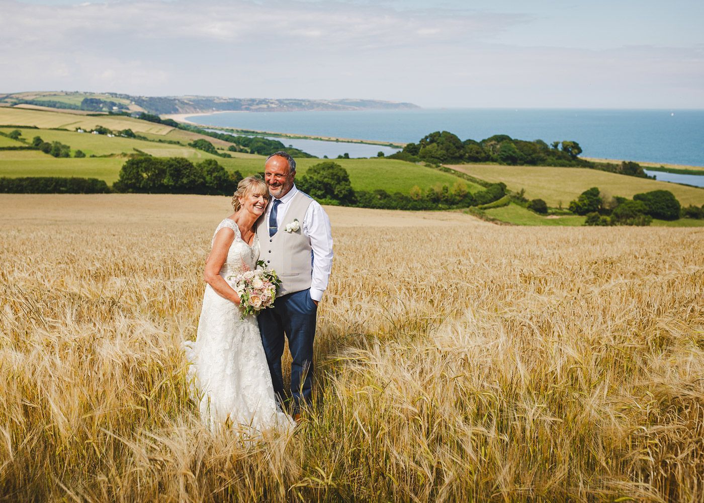 A bride and groom are standing in a field of wheat.