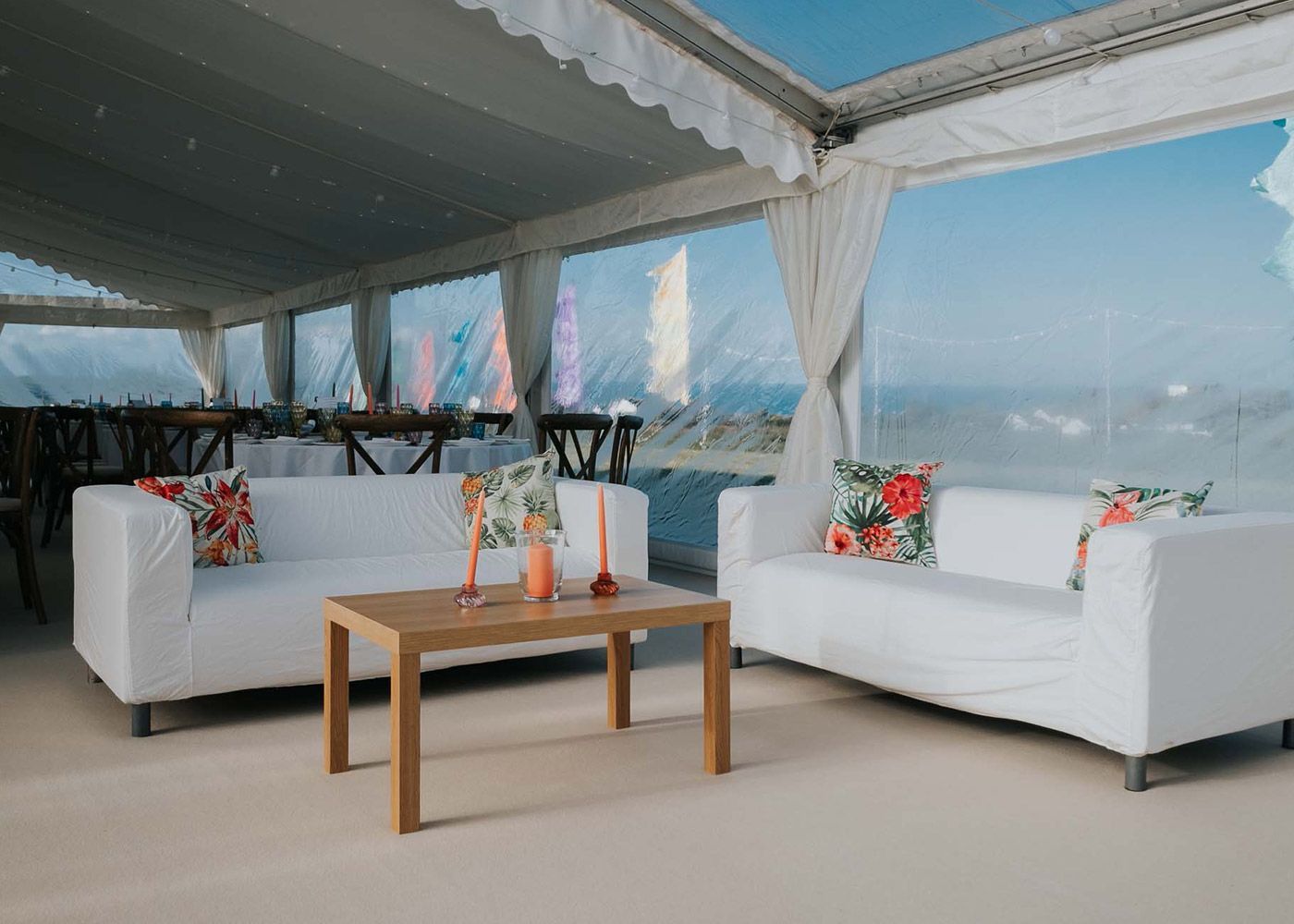 Two white couches are sitting next to a wooden table under a tent.