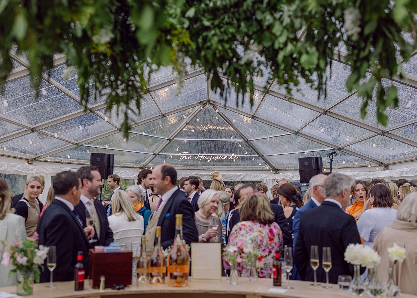 A group of people are standing around a bar under a clear tent.