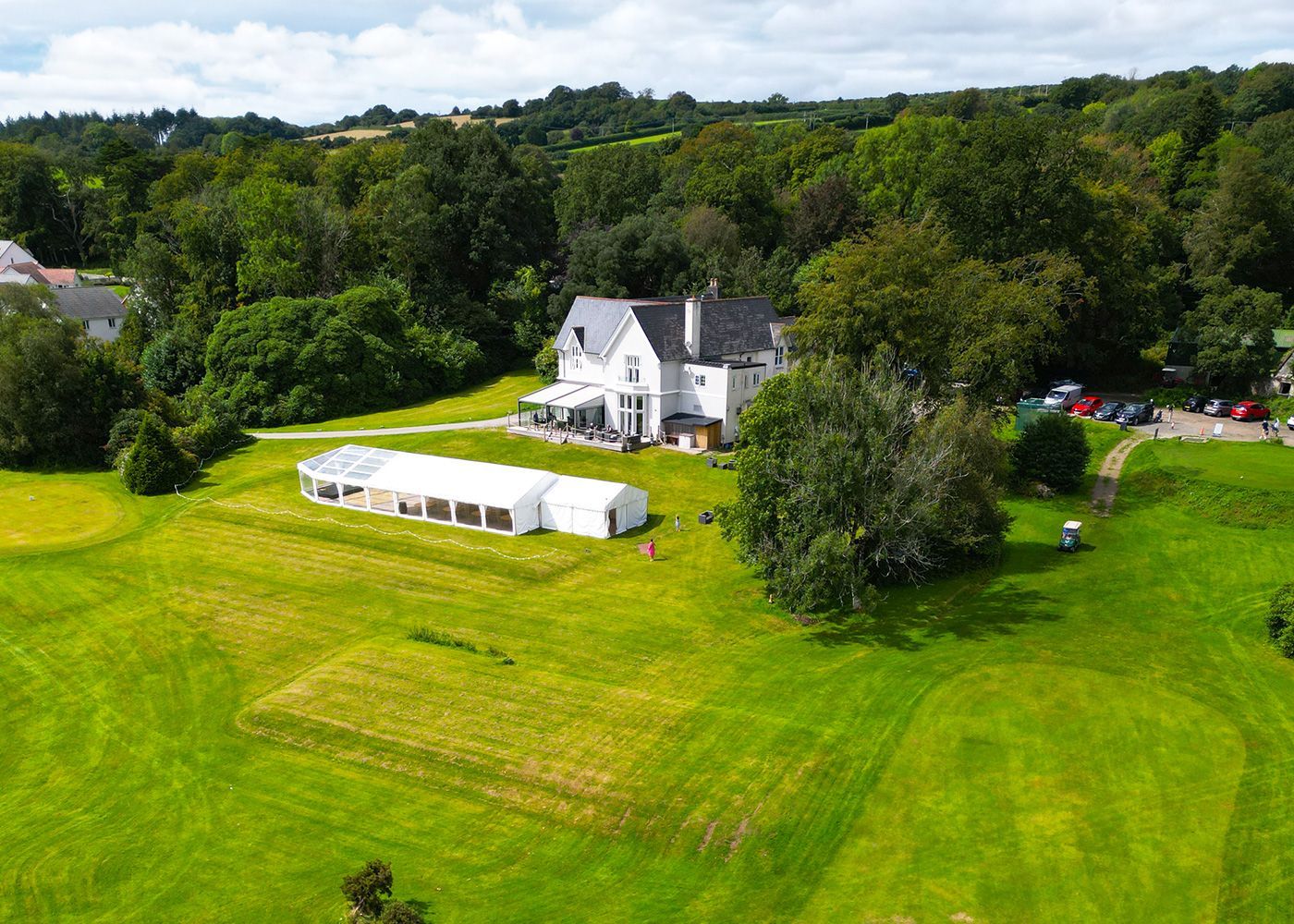 An aerial view of a large house in the middle of a lush green field.
