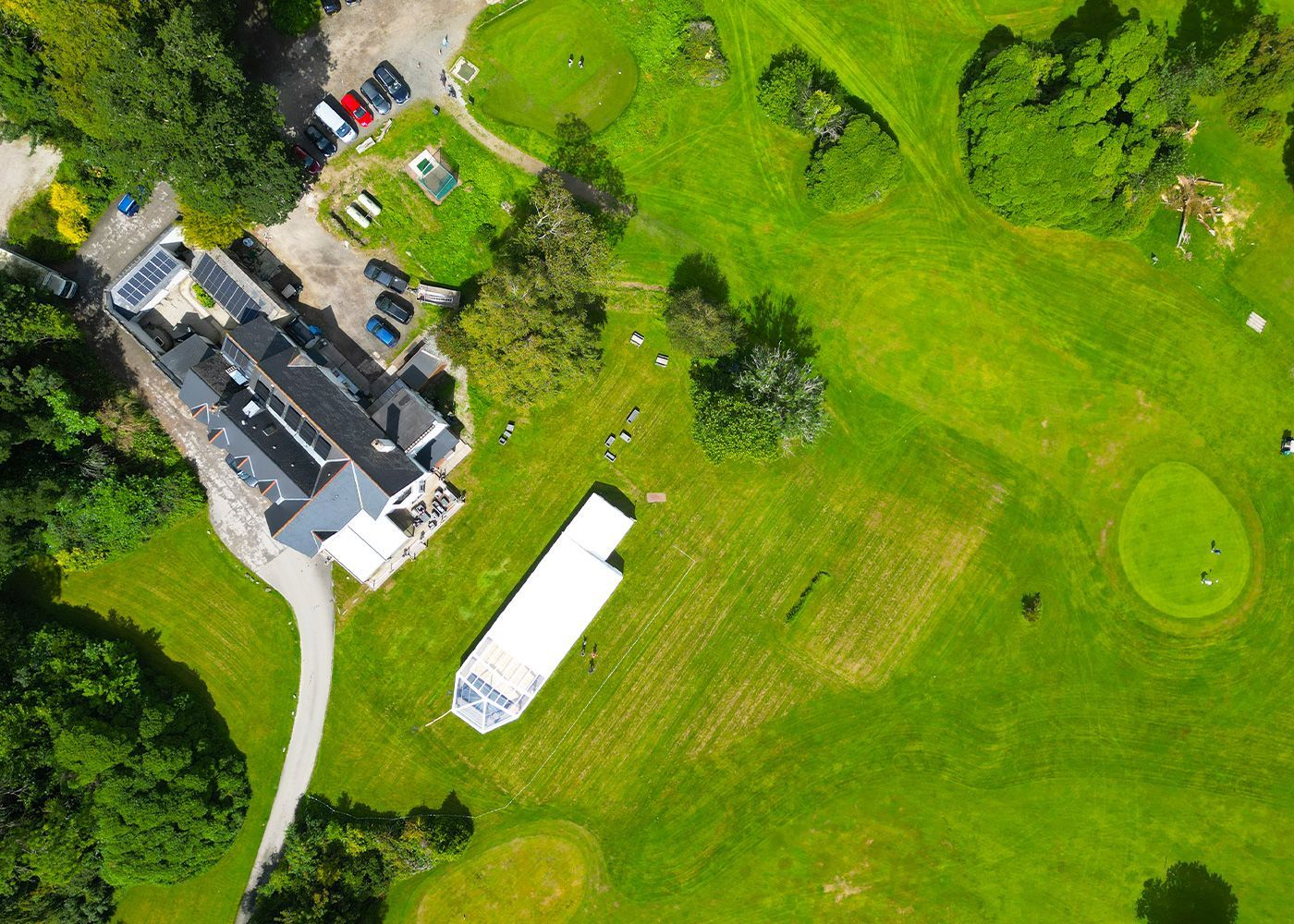 An aerial view of a golf course with a white tent in the middle of it.