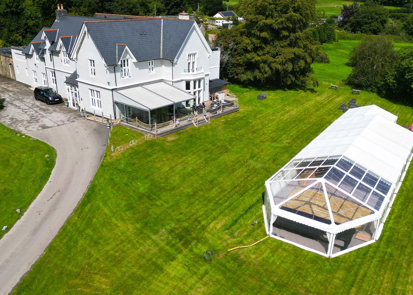 An aerial view of a large white house with a clear tent in front of it.