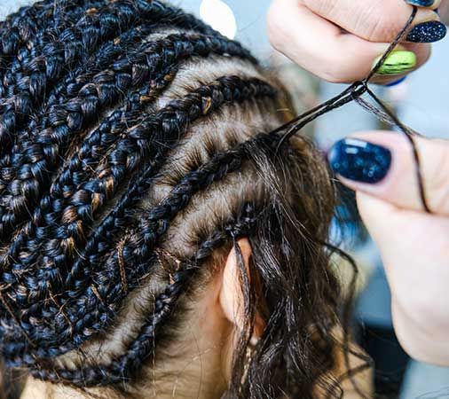 Hands braiding hair with black extensions. Close-up view of a person's head, the process is underway.