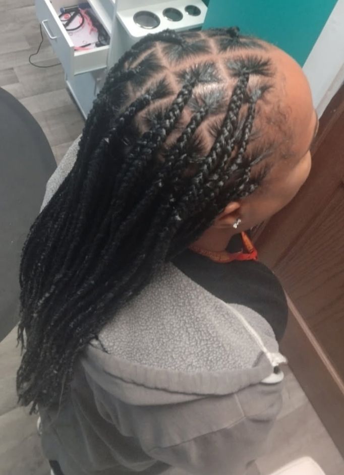 Person with black braids and a diamond pattern at the top of their head, wearing a gray hoodie.