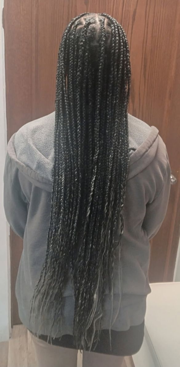 Person with long box braids, wearing a gray hooded sweatshirt. Standing in front of a wood door.