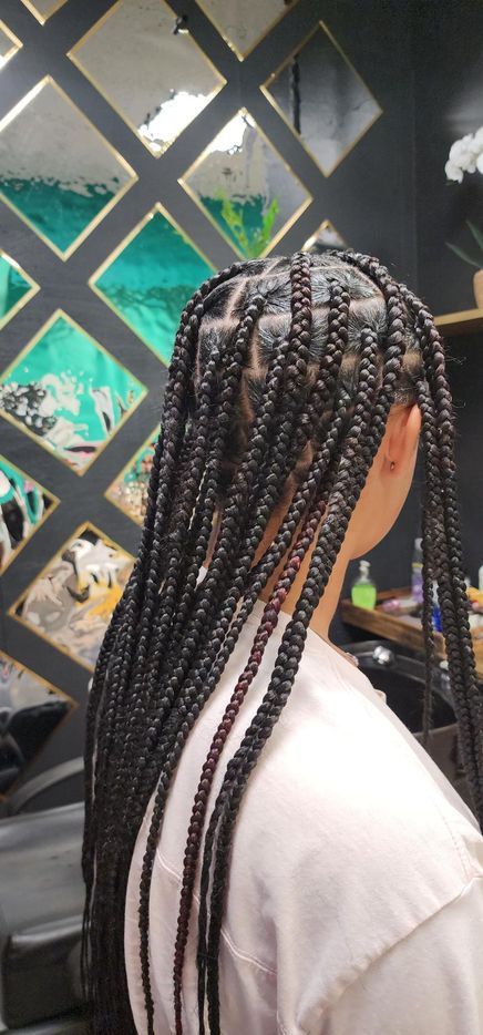 Person with dark hair in box braids, turned away. Braids are long and thick. Light-colored top.