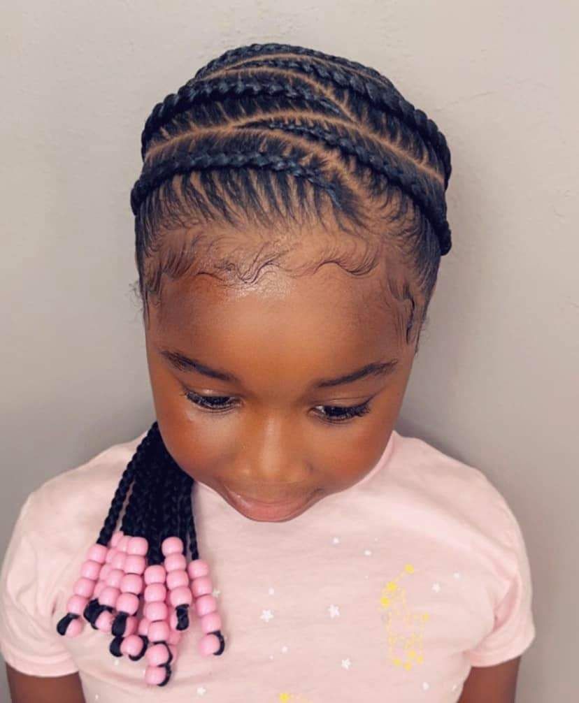 Woman with blonde dreadlocks, zebra-print top, tying hair up, against a white slatted wall.