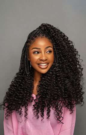 Young Black woman with curly dark hair smiling. She's wearing a pink shirt, and her hair is partially braided.