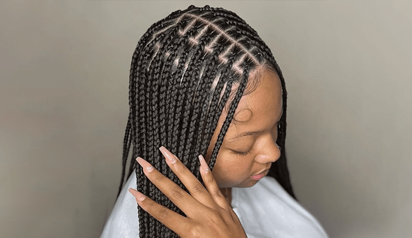 Woman with box braids, hand resting on hair. Braids are black with a square design.