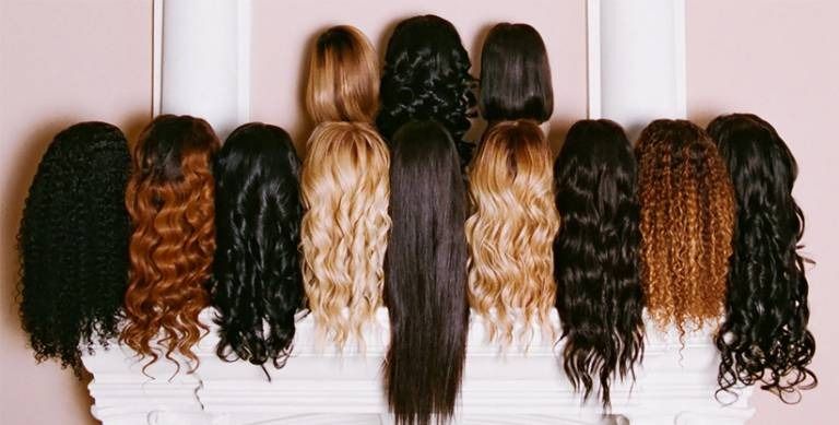 Collection of various wigs, showcasing different styles and colors against a pink wall.