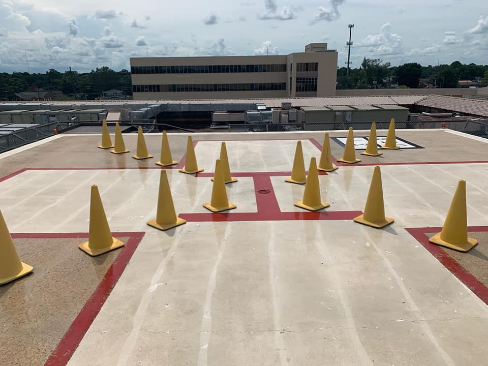 Yellow traffic cones arranged on a rooftop helipad, near a large building.