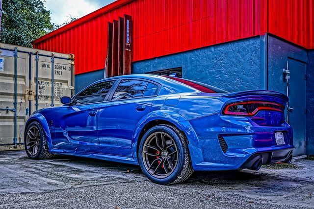 A blue dodge charger is parked in front of a red building.