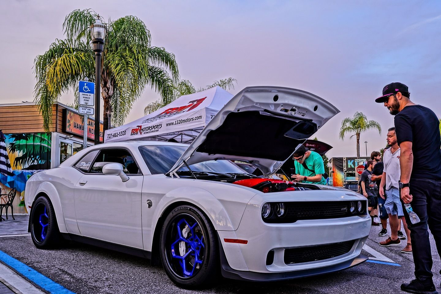 A man is standing next to a white car with the hood up.