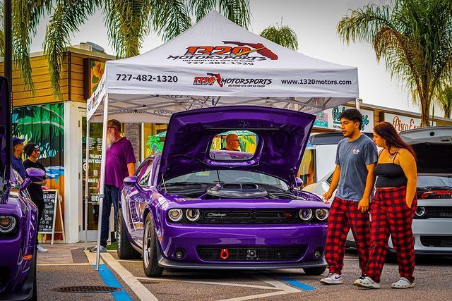 A group of people are standing in front of a purple car with the hood up.