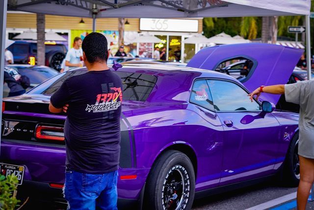 A man is standing next to a purple car with the hood up.
