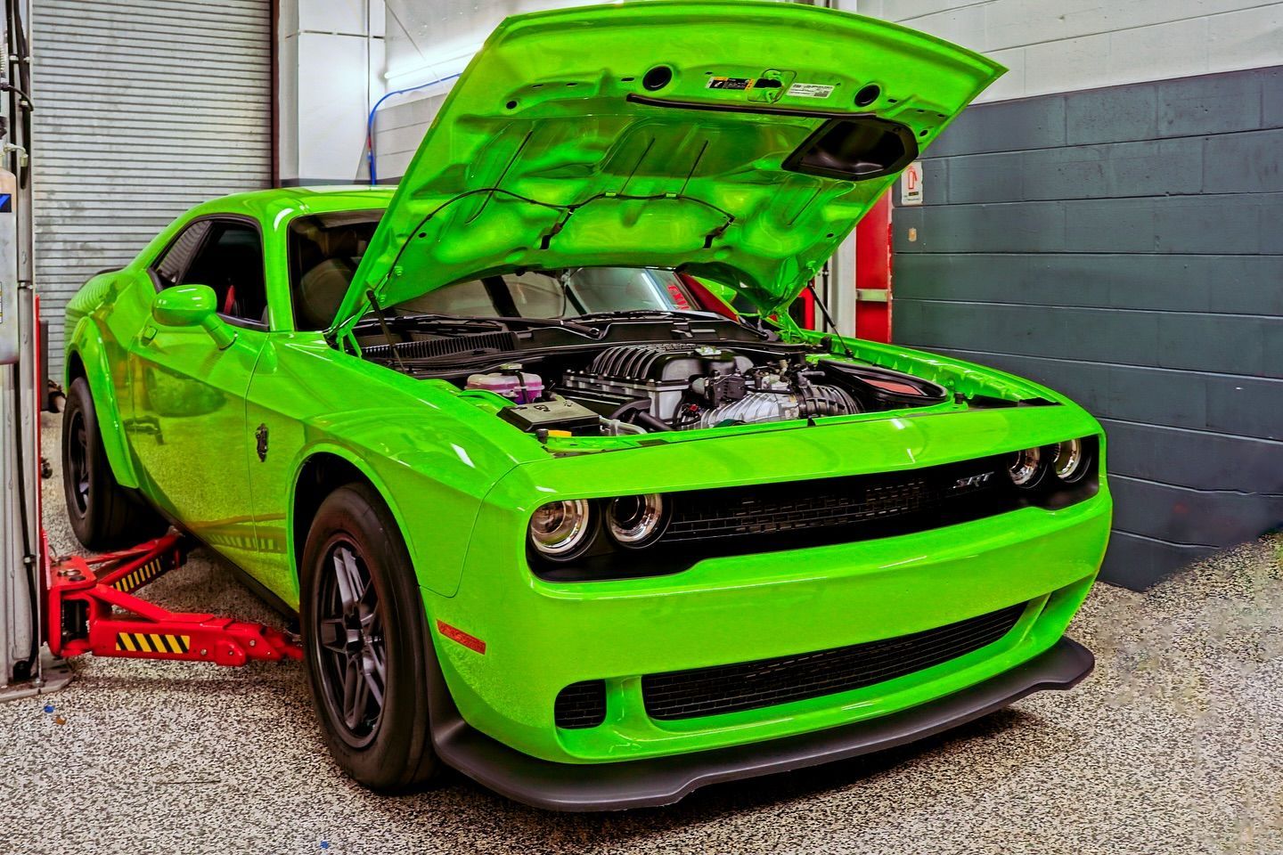 A green dodge challenger with the hood open is parked in a garage.