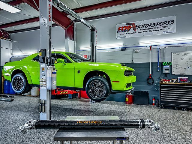 A green dodge challenger is on a lift in a garage.
