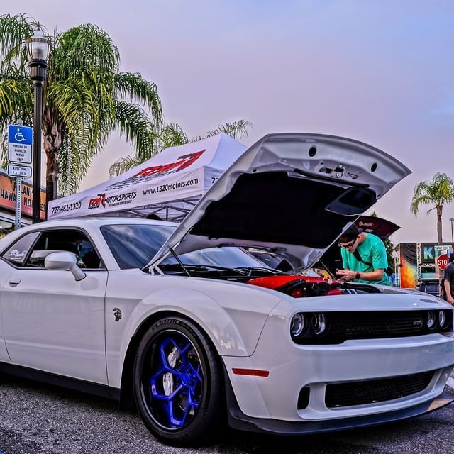 A white car with the hood up is parked on the street