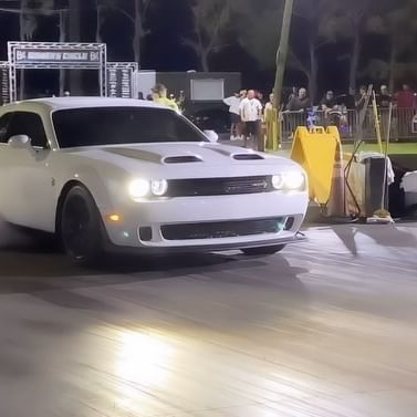 A white dodge challenger is driving down a track at night.