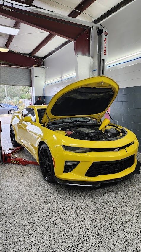 A yellow car with the hood open is parked in a garage.