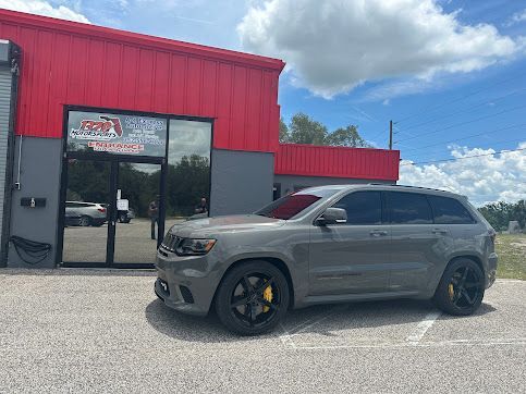A gray jeep grand cherokee is parked in front of a red building.
