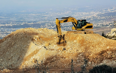 Yellow excavator loading dirt into a red dump truck, against a blue sky.
