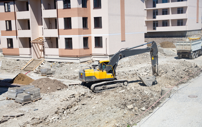 Yellow excavator loading dirt into a red dump truck, against a blue sky.