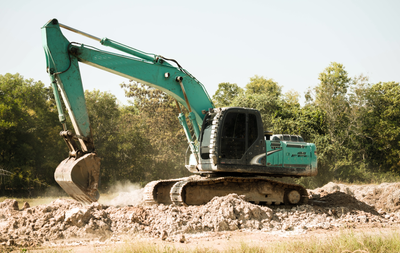 Yellow excavator loading dirt into a red dump truck, against a blue sky.