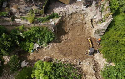 Yellow excavator loading dirt into a red dump truck, against a blue sky.