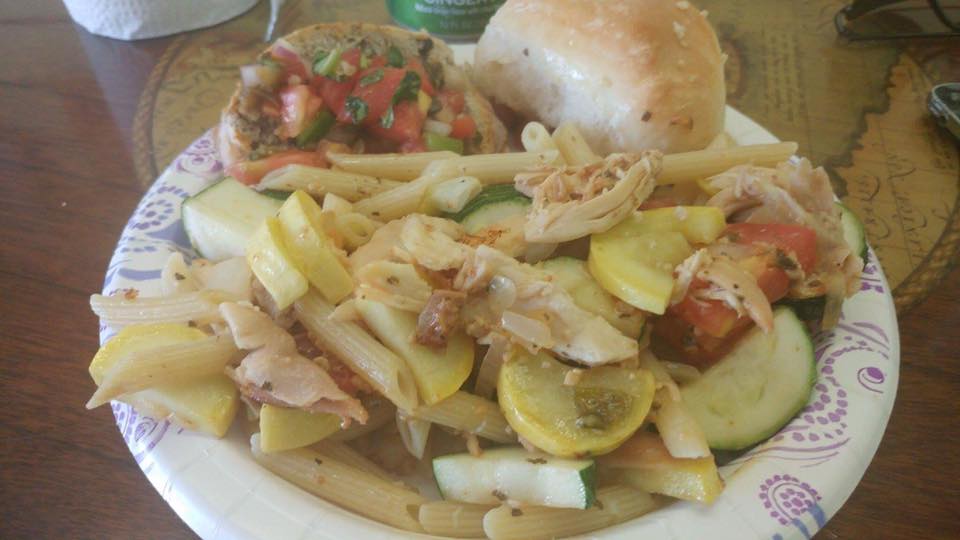Pasta, squash, tomatoes, and bread on a paper plate.