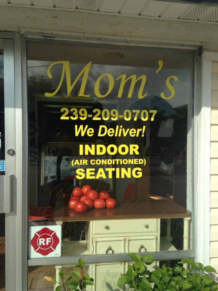 Window sign for Mom's restaurant with delivery, phone number, and indoor seating; tomatoes and cabinet visible inside.