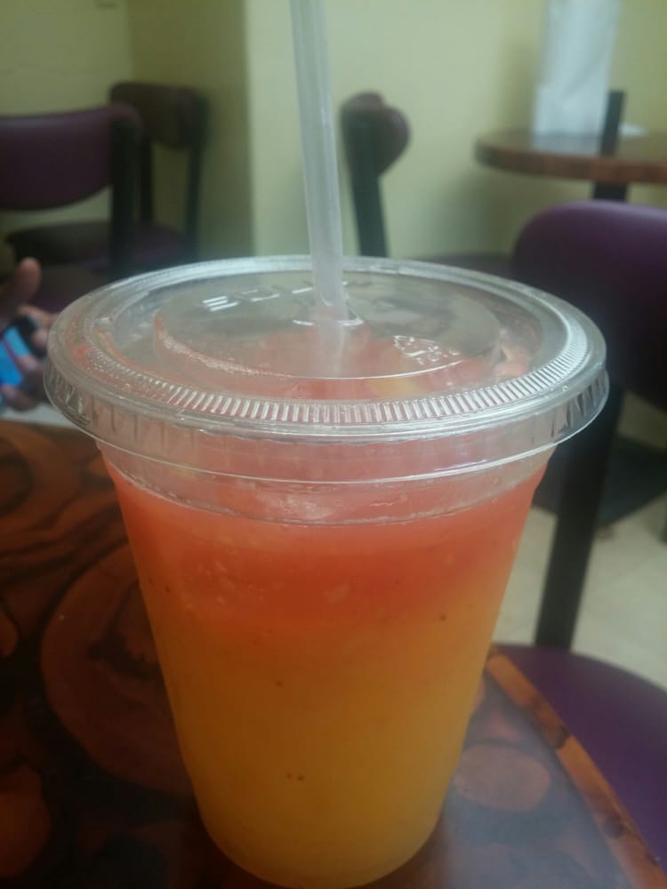 Orange and red layered drink in a clear plastic cup with a straw on a table.