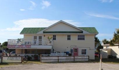 Two-story yellow building with green roof, white railings, and a pink door under a blue sky.