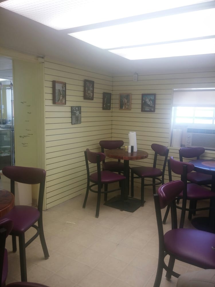 Interior of a small cafe with round tables, purple chairs, and framed photos on the wall.