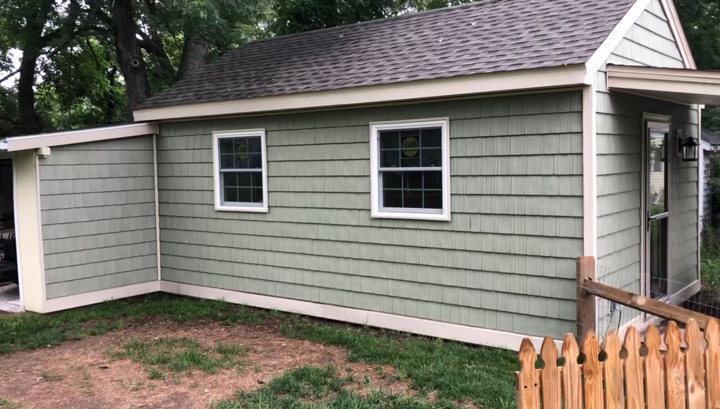 A small green house with a wooden fence in front of it.